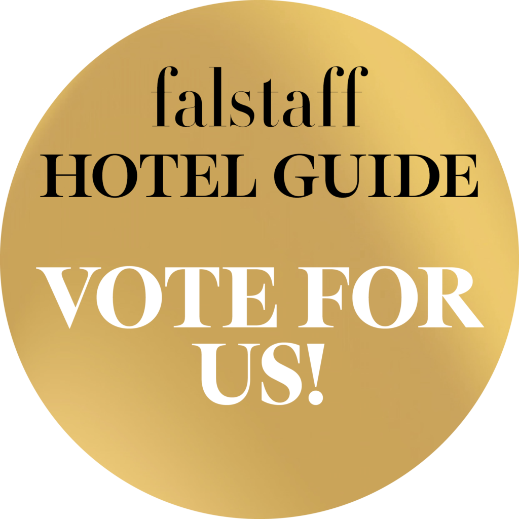 Ein goldenes rundes Badge mit dem Text „Falstaff Hotel Guide“ in Schwarz und „Vote for Us!“ in fetten weißen Lettern.