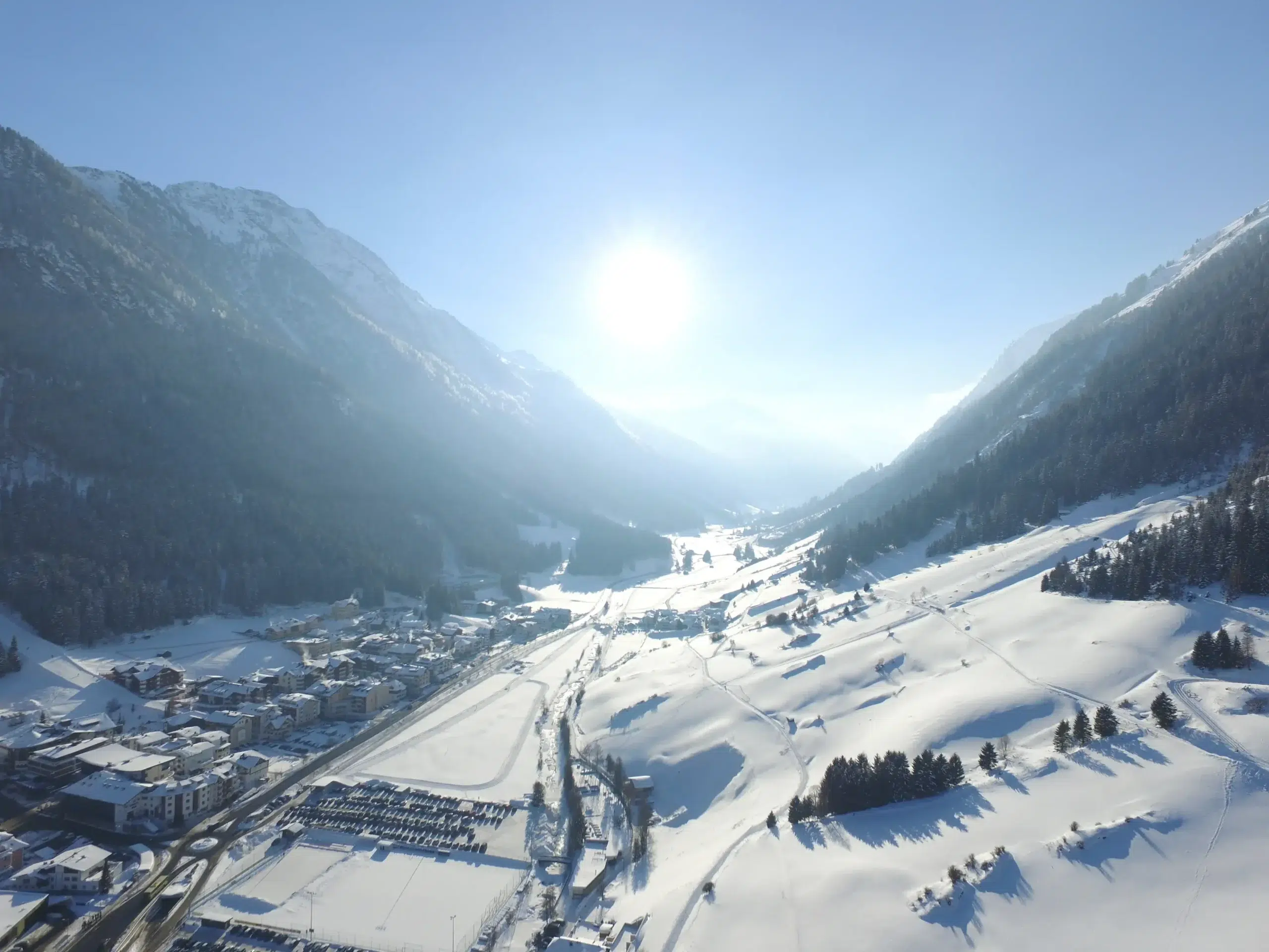A snowy mountain valley with a village under a bright sun and clear blue sky.