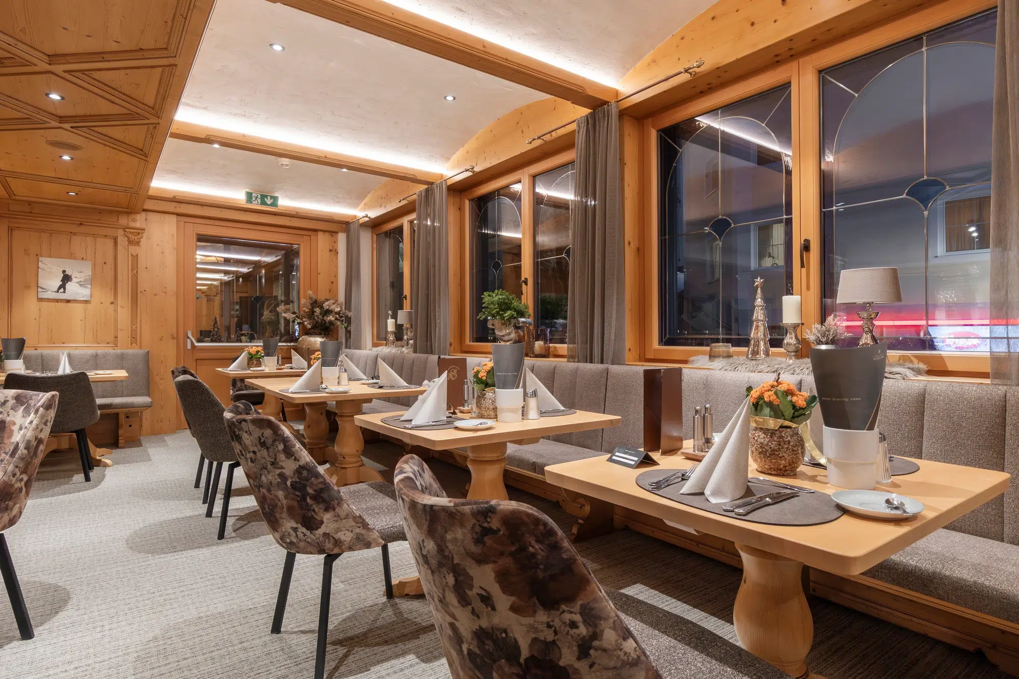 Elegant restaurant with wooden decor, set tables, and upholstered chairs, softly lit at night.