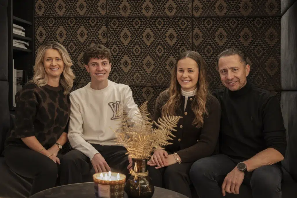 Family Zangerl Ischgl sit closely together on a couch, smiling, with a candle and vase on the table.